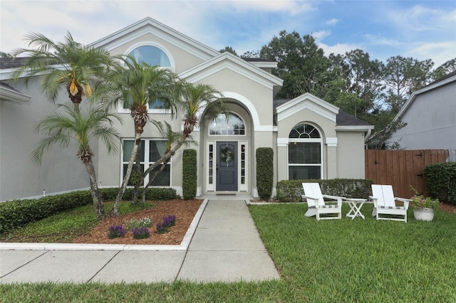 doorway to property featuring fence, stucco siding, and a yard