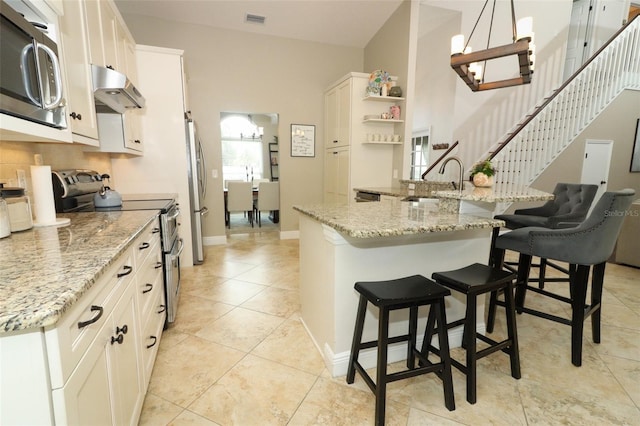 kitchen featuring a sink, a breakfast bar area, stainless steel appliances, under cabinet range hood, and visible vents