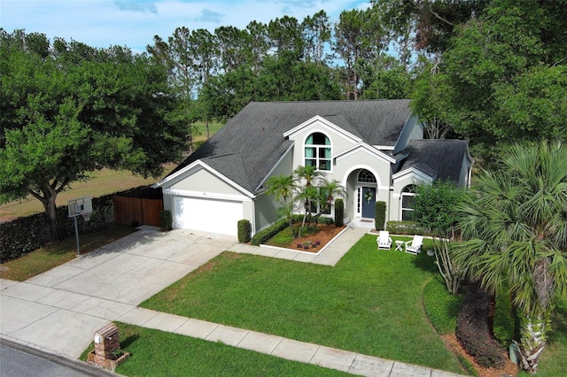 view of front facade featuring roof with shingles, an attached garage, stucco siding, a front yard, and concrete driveway