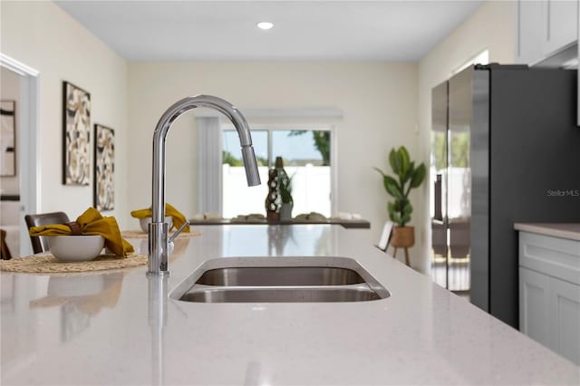 kitchen with light stone countertops, recessed lighting, a sink, open floor plan, and refrigerator with ice dispenser