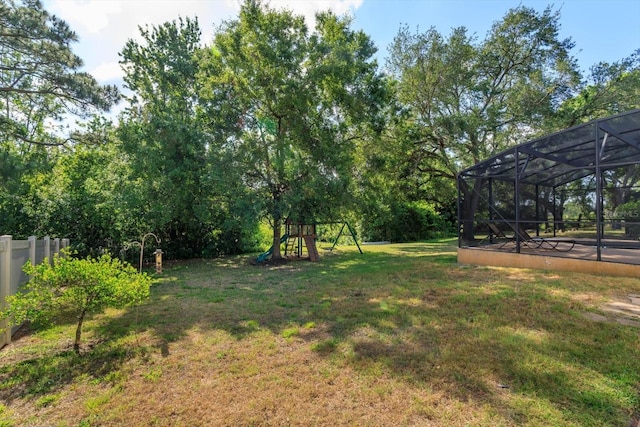 view of yard with a playground, glass enclosure, and fence