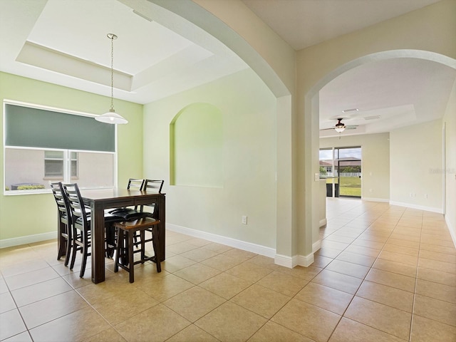 dining room with ceiling fan, arched walkways, light tile patterned floors, baseboards, and a tray ceiling