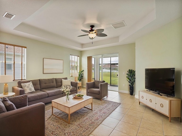 living room with visible vents, baseboards, a tray ceiling, a ceiling fan, and light tile patterned floors