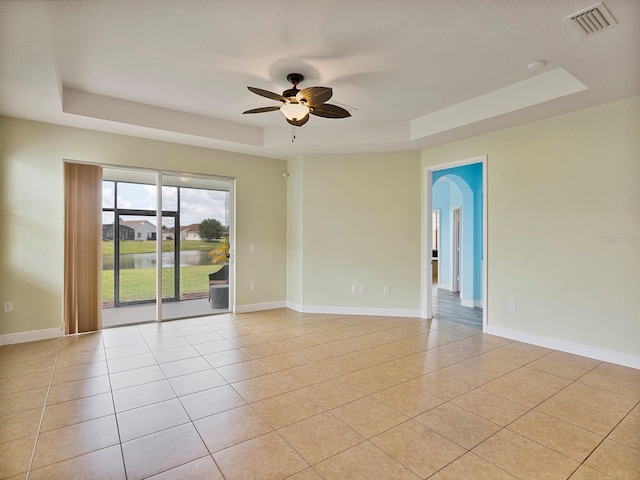 spare room with a ceiling fan, visible vents, light tile patterned floors, a raised ceiling, and a water view