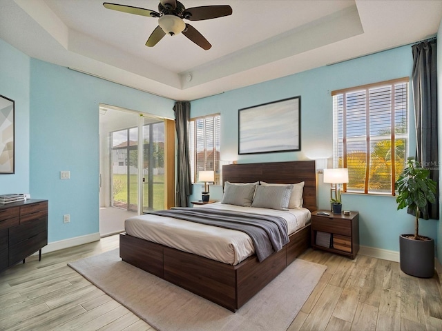 bedroom featuring baseboards, access to outside, a tray ceiling, and light wood-style flooring