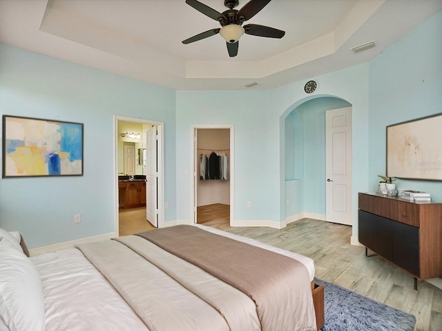 bedroom featuring visible vents, arched walkways, a raised ceiling, a spacious closet, and light wood-style flooring