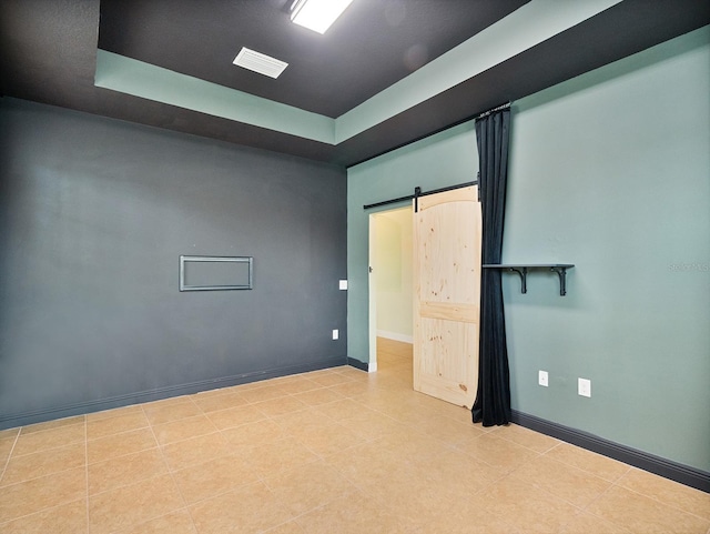 spare room featuring visible vents, tile patterned flooring, a barn door, a raised ceiling, and baseboards