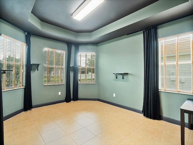 unfurnished room with tile patterned flooring, a raised ceiling, baseboards, and a healthy amount of sunlight