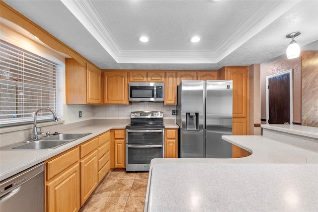 kitchen featuring a sink, a tray ceiling, light countertops, appliances with stainless steel finishes, and ornamental molding