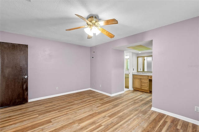 interior space with built in desk, ensuite bathroom, light wood finished floors, a ceiling fan, and baseboards