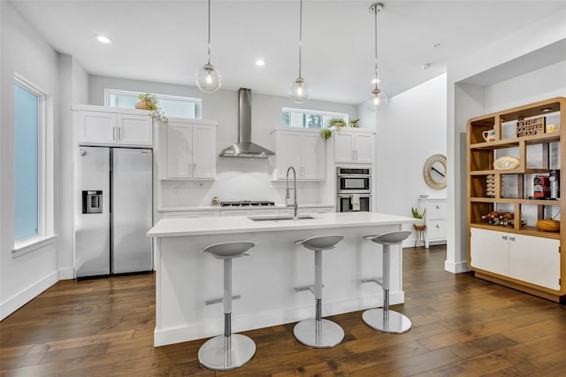 kitchen with a sink, stainless steel appliances, wall chimney range hood, dark wood finished floors, and light countertops