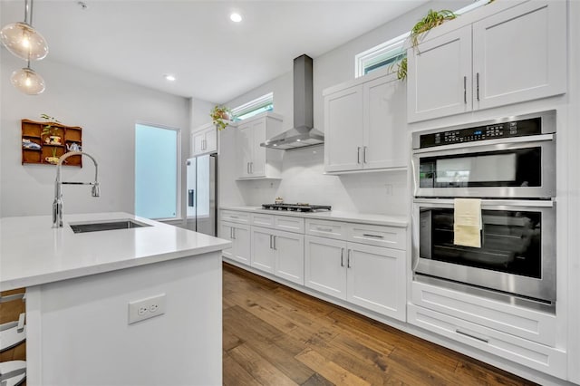 kitchen featuring recessed lighting, a sink, wall chimney range hood, light countertops, and appliances with stainless steel finishes