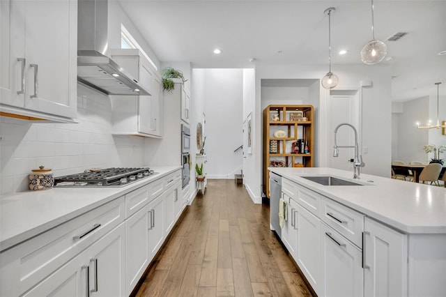 kitchen with recessed lighting, a sink, backsplash, wall chimney range hood, and appliances with stainless steel finishes