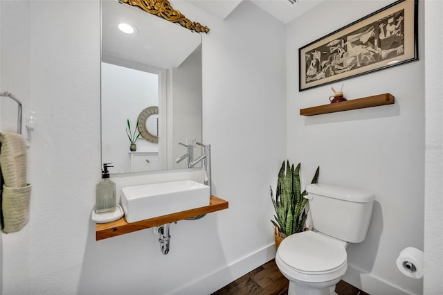 half bath featuring toilet, baseboards, a sink, and wood finished floors