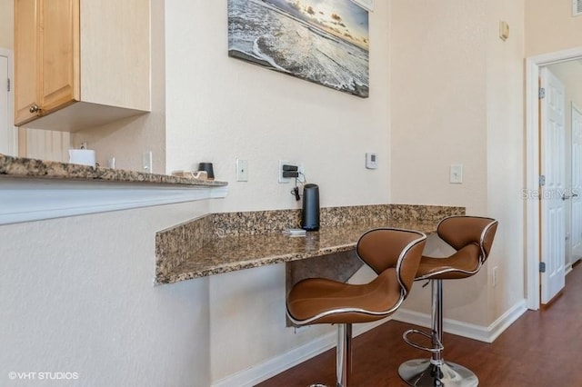 kitchen featuring baseboards, stone counters, light brown cabinetry, and dark wood-style floors