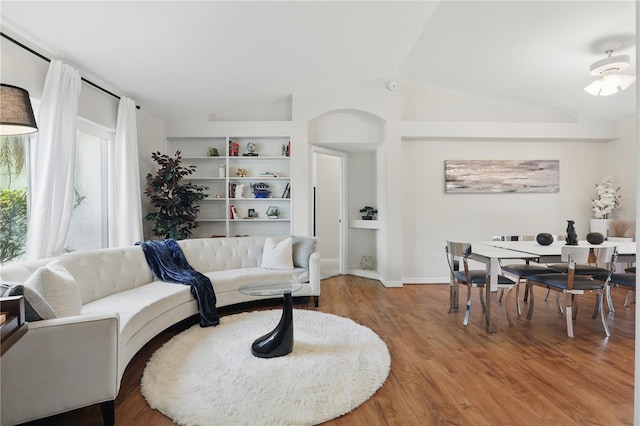 living area with baseboards, built in features, wood finished floors, and vaulted ceiling