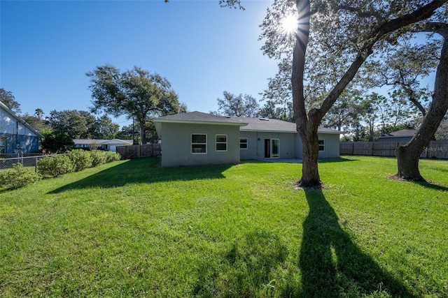 back of house with stucco siding, a yard, and a fenced backyard