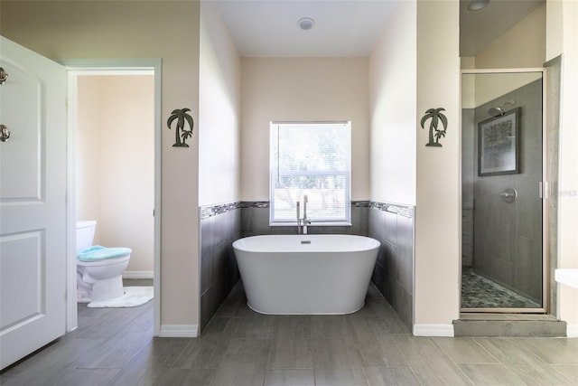 bathroom featuring toilet, a stall shower, a wainscoted wall, and a freestanding bath