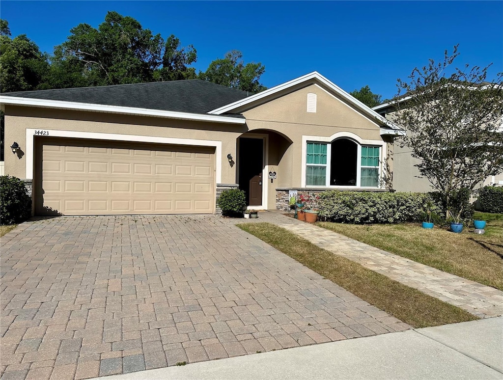 ranch-style home with an attached garage, decorative driveway, and stucco siding