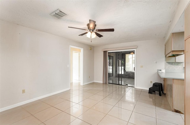 interior space with a ceiling fan, a textured ceiling, visible vents, light tile patterned floors, and baseboards