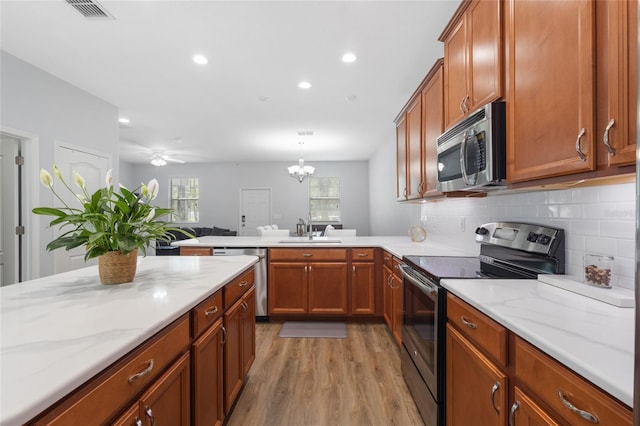 kitchen featuring brown cabinets, a sink, a peninsula, light wood finished floors, and stainless steel appliances