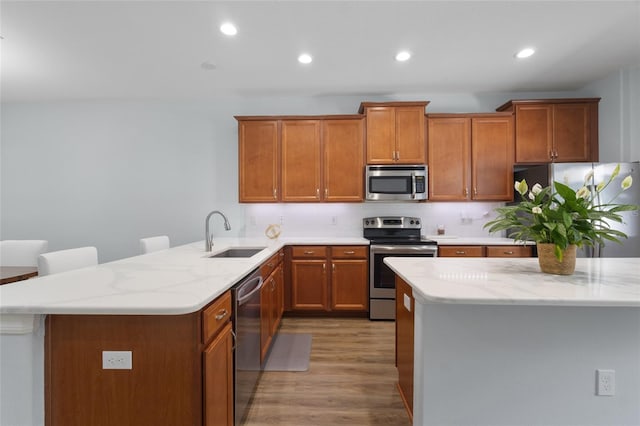 kitchen with a sink, light wood-style floors, stainless steel appliances, and brown cabinets