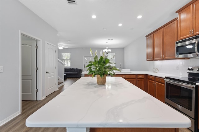 kitchen with brown cabinetry, appliances with stainless steel finishes, wood finished floors, a sink, and recessed lighting