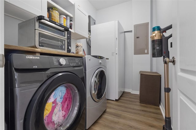 laundry room with baseboards, light wood-type flooring, electric panel, washing machine and clothes dryer, and cabinet space