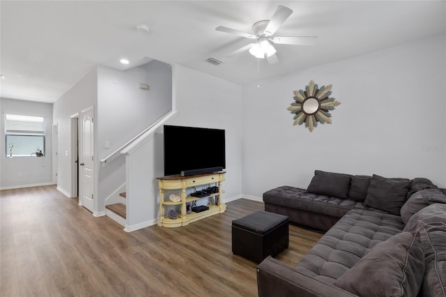 living room featuring ceiling fan, visible vents, wood finished floors, baseboards, and stairs