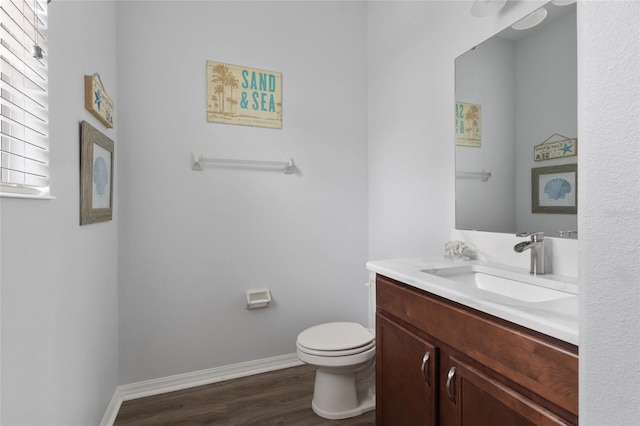 half bathroom with vanity, baseboards, wood finished floors, and toilet