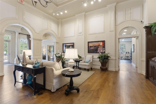 living room featuring decorative columns, a towering ceiling, crown molding, arched walkways, and hardwood / wood-style flooring