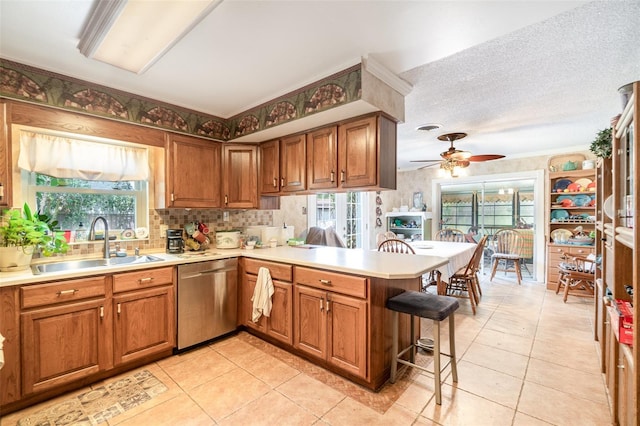 kitchen with a breakfast bar, a sink, a peninsula, a ceiling fan, and stainless steel dishwasher