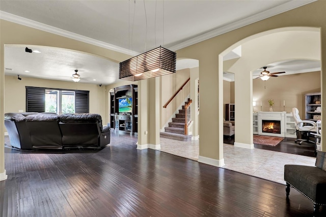 living room featuring stairs, a warm lit fireplace, ceiling fan, and hardwood / wood-style flooring