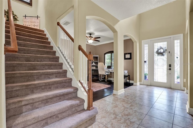 entryway with arched walkways, stairs, a ceiling fan, baseboards, and light tile patterned floors