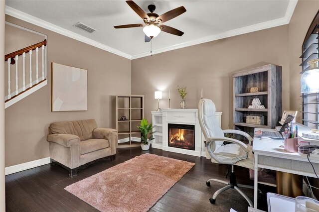 home office with crown molding, ceiling fan, a glass covered fireplace, baseboards, and wood finished floors