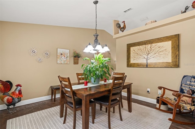 dining room with an inviting chandelier, baseboards, wood finished floors, lofted ceiling, and visible vents