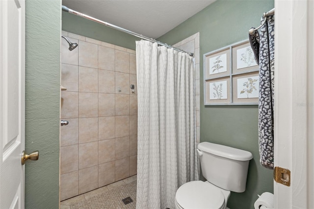 bathroom featuring toilet, tiled shower, and tile patterned flooring