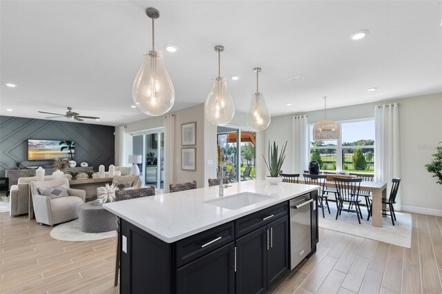 kitchen with an island with sink, light countertops, a sink, light wood-style flooring, and dishwasher