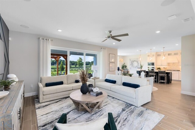 living room featuring visible vents, a ceiling fan, light wood-style flooring, and baseboards
