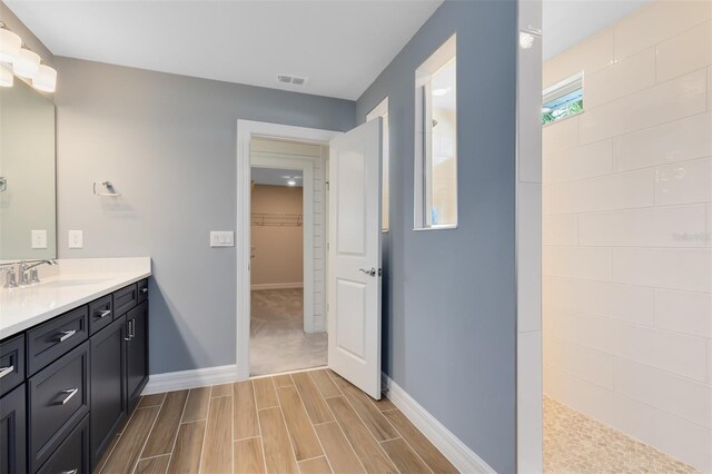 bathroom with wood tiled floor, visible vents, walk in shower, vanity, and baseboards