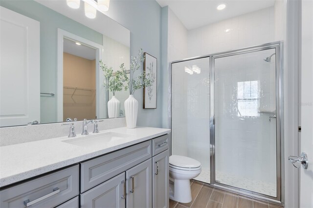 full bath with a walk in closet, a shower stall, wood finished floors, vanity, and toilet