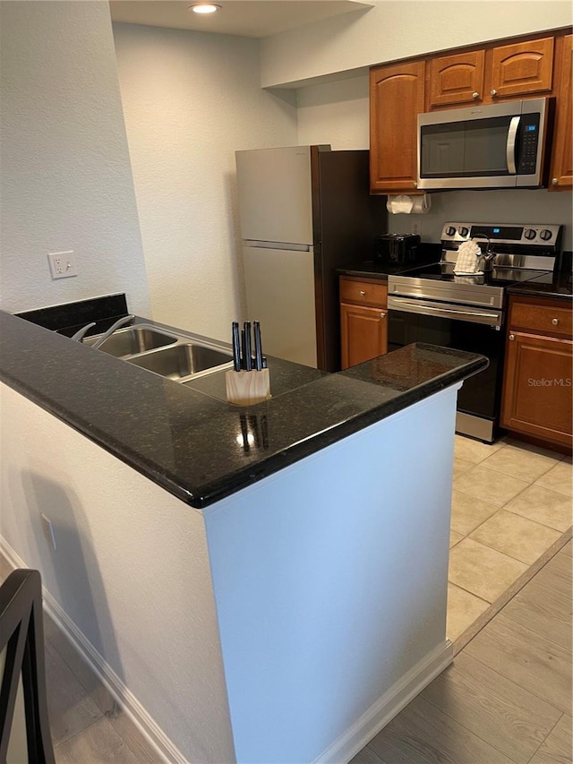 kitchen with a sink, appliances with stainless steel finishes, brown cabinets, and a peninsula