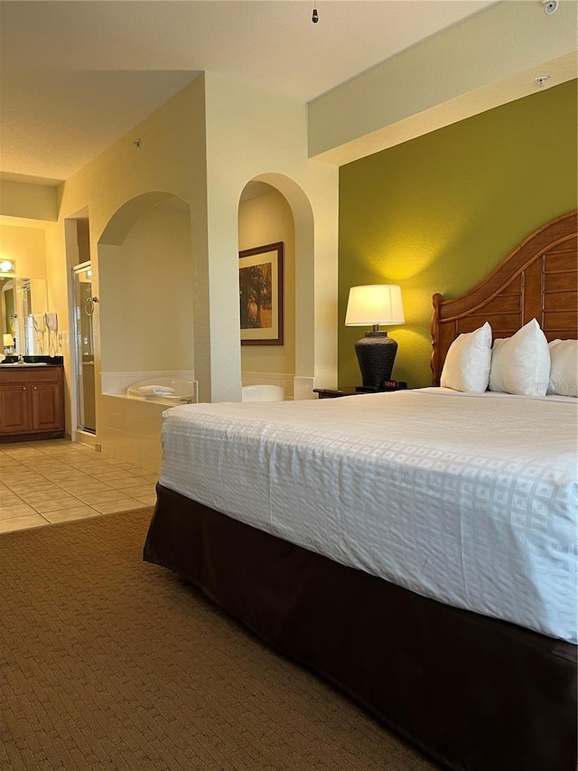 bedroom featuring arched walkways, light tile patterned floors, and ensuite bathroom
