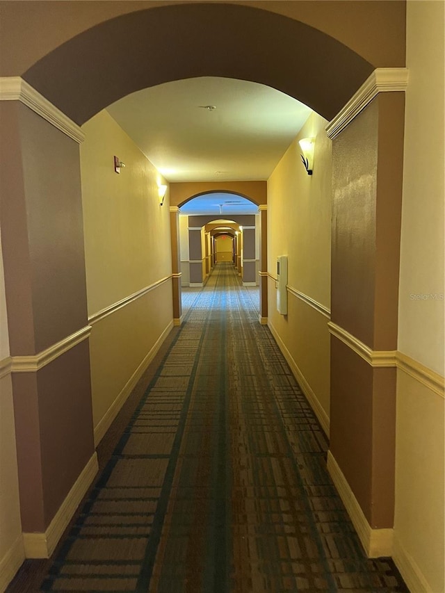 hallway with arched walkways, baseboards, and carpet
