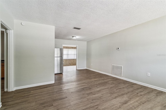 empty room featuring a textured ceiling, visible vents, baseboards, and dark wood-type flooring