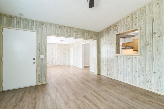 empty room featuring a ceiling fan, wallpapered walls, wood finished floors, and lofted ceiling
