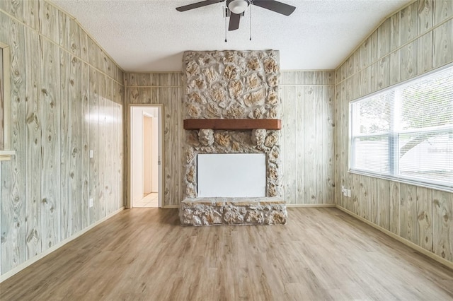 unfurnished living room with wooden walls, a textured ceiling, ceiling fan, and wood finished floors
