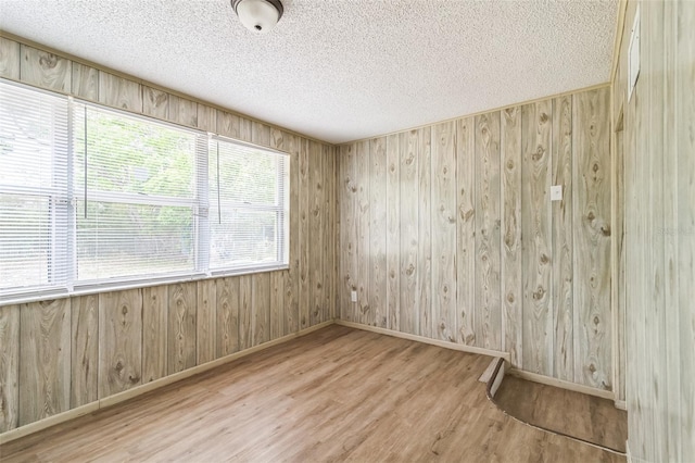 empty room featuring baseboards, wood walls, a textured ceiling, and wood finished floors