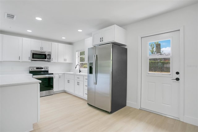 kitchen with a sink, stainless steel appliances, light wood-type flooring, visible vents, and white cabinets