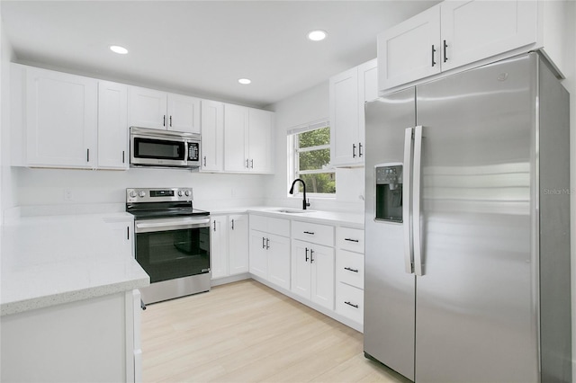 kitchen featuring light wood-style flooring, light stone counters, appliances with stainless steel finishes, a sink, and white cabinetry